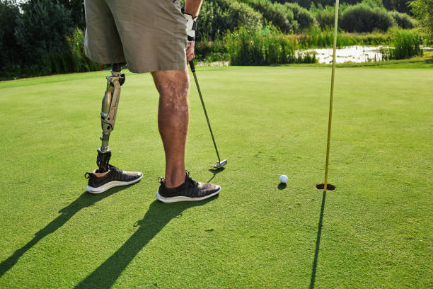 profigolfer mit beinprothese, die beim golfen an sonnigen tagen mit langen schatten mit putter auf golfball schlägt - amputiert stock-fotos und bilder