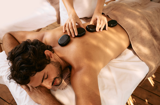 Hombre guapo en el complejo de spa recibe masaje con piedras calientes. Terapia de masaje con piedras calientes con piedras lisas, planas y calentadas photo