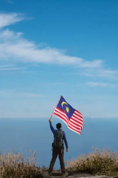 Male hiker on a mountain top holding Malaysian flag.