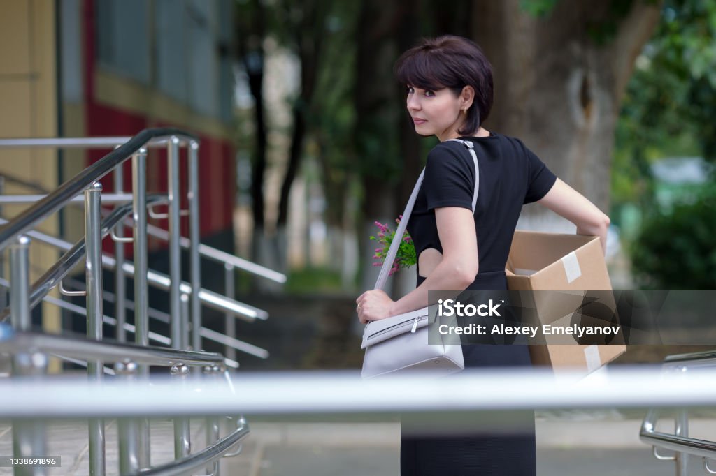 A happy brunette in a black dress with a box of personal belongings is in a hurry for a new job, an employment concept A happy brunette in a black dress with a box of personal belongings is in a hurry for a new job employment concept. 35-39 Years Stock Photo
