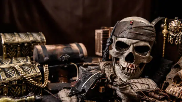 Photo of Pirate with human skull. Treasure chest and gold. Discovery equipment and explorer for disappear fortune.