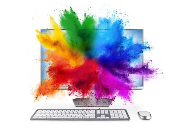 modern black silver pc monitor with mouse and keyboard colorful rainbow holi powder cloud explosion through screen isolated on white background. computer multimedia abstract art streaming concept.