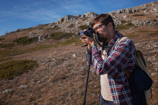 istock Young man taking photographs with digital camera in a mountains. 1338698813
