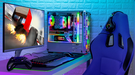 colorful bright illuminated rgb gaming pc with keyboard mouse monitor and chair with racing on screen in front of LED light brick stone wall. Computer playing hardware games background