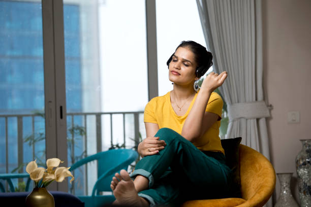 Woman enjoying her favourite music using headphones Beautiful woman enjoying her favourite music using headphones at home woman sitting cross legged in chair stock pictures, royalty-free photos & images