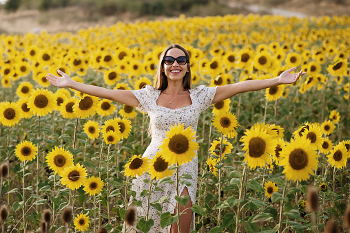 Cheerful young woman with arms raised in a sunflower field