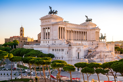 A suggestive sunset view of the Campidoglio or Capitoline Hill (Left), the ancient seat of the Roman Capitol, and the National Monument of the Altare della Patria (center), in the historic heart of Rome. Below, surrounded by the pine trees, the Imperial Forums Boulevard. The Capitoline Hill, one of the seven hills of Rome, was considered the sacred place for the Romans, between the Forum and the Campus Martius, where the majestic Temple of Capitoline Jupiter was erected. Currently the Palazzo del Campidoglio, with its characteristic bell tower, is the seat of the Municipality of Rome (Town Hall). The national monument of the Altare della Patria, or Vittoriano, was built in 1885 in neoclassical style in honor of the first King of Italy, Vittorio Emanuele II, between the north side of the Capitoline Hill and the central Piazza Venezia. Inside is the Tomb of the Unknown Soldier, a War Memorial dedicated to all the Italian soldiers who died in the war. The Altare della Patria is the scene of all the official Italian civic celebrations, in particular the Republic Day on June 2 and the Liberation Day on April 25. In 1980 the historic center of Rome was declared a World Heritage Site by Unesco. Image in high definition format.