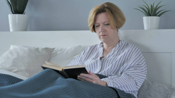 istock Old Woman Reading Book while Sitting in Bed 1338704427