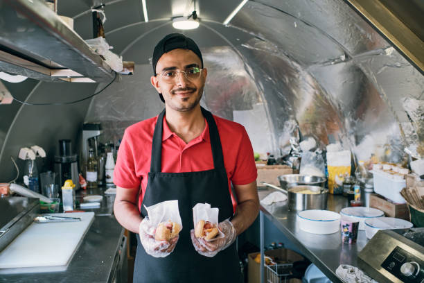 Gloved young man in uniform holding fast food Gloved young man in uniform holding fast food while standing inside truck fast food restaurant stock pictures, royalty-free photos & images