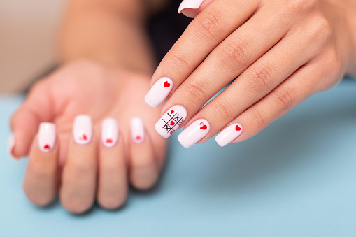 Beautiful female hands with romantic manicure nails, hearts and Valentine's day design, on blue background