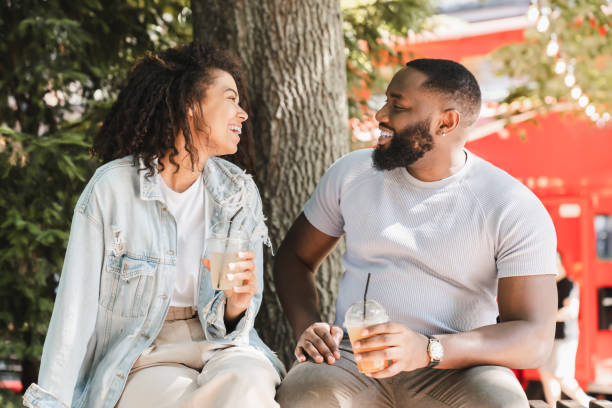 istock African-american romantic couple having romantic date, drinking lemonade while sitting talking communicating in park outdoors. Love and relationship, bonding concept 1338710520