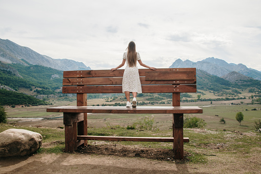 Young woman contemplating a beautiful landscape on a giant bench in a mountain area