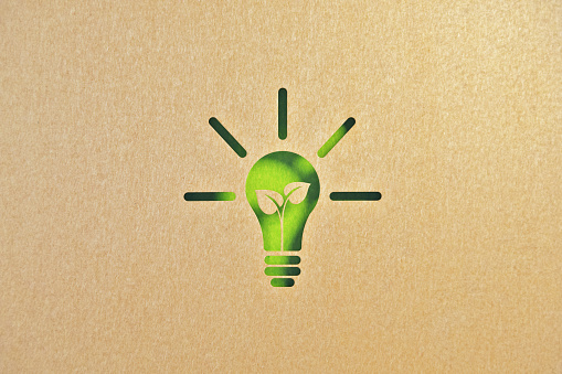 Cut out light bulb made of recycled paper on green background. Horizontal composition with copy space. Sustainability and renewable energy concept.