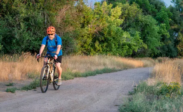 senior male cyclist is riding a touring bike on a gravel trail at Colorado foothills, late summer scenery