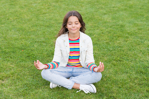 kid meditating in yoga pose on grass. child in lotus pose on green grass. Concept of calm and meditation. meditation in nature. peace and relax. small girl meditate in summer park. healthy lifestyle.