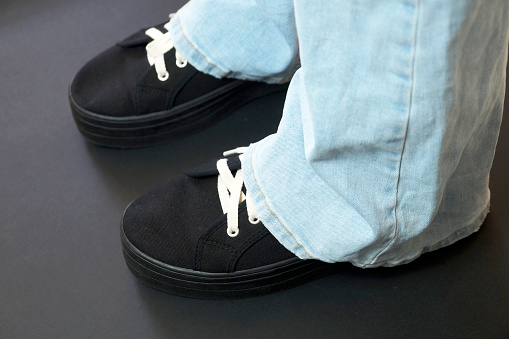 female legs in blue jeans and black sneakers on a black background.