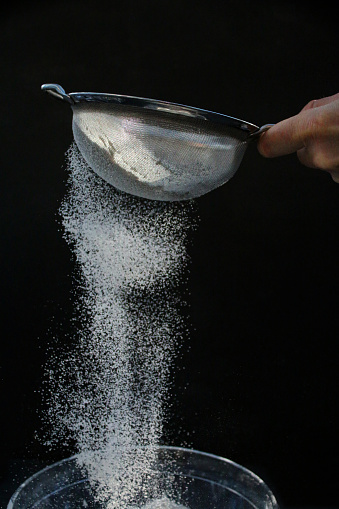 Stock photo showing close-up view metal sieve holding by an unrecognisable person, using it to sieve white flour.