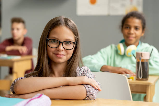 urocza uczennica w okularach patrząca na ciebie przy biurku - child glasses eyewear little girls zdjęcia i obrazy z banku zdjęć