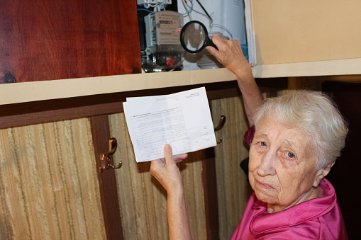 Terrified senior poor woman is checking electricity meter - consumption and expensive electricity concept