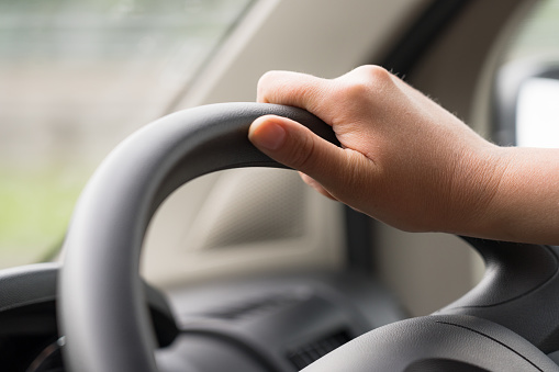A close-up of a woman's hand as she holds the steering wheel on a long journey.