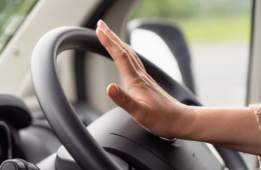Close-up of a woman's hand as she presses the car's horn button on the centre of the steering wheel.