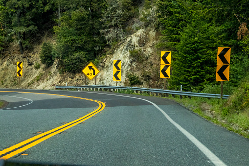 Curve on two laned highway in USA with hill on one side and many  curve road signs