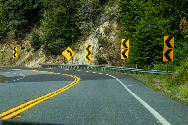 curve on two laned highway in usa with hill on one side and many  curve road signs - arrow sign road sign fence imagens e fotografias de stock