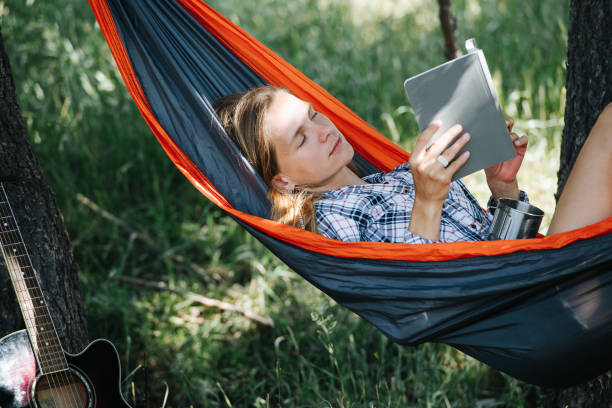 istock Reading woman lying in a hammock, in a shadow, between two big trees. 1338725514