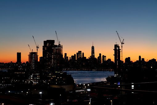 Construction cranes line the city skyline at dusk in New York City.