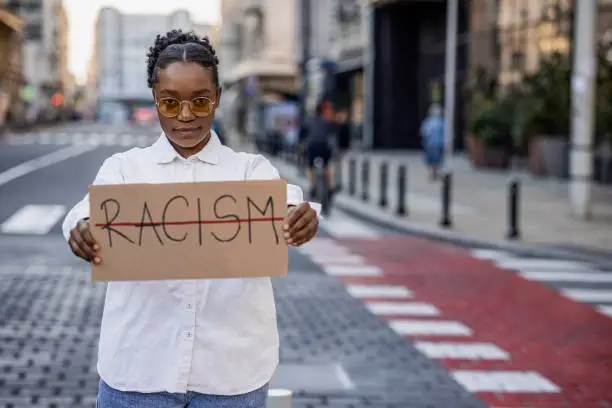 Portrait of young woman on the street, holding a sign against racism