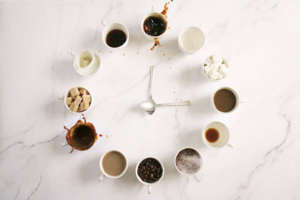 Image of white, espresso cup clock face design , sugar cubes, milk, coffee and coffee beans in cups, teaspoon clock hands, overflowing, spraying, splashing droplets floating mid-air,  marble effect background, elevated view, copy space stock photo