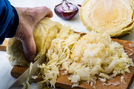 Male hand slicing sour cabbage on a cutting board for a winter salad. Sauerkraut is finely cut raw cabbage that has been fermented by various lactic acid bacteria