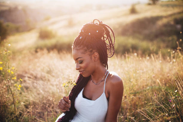 Beautiful black young woman in the park portrait long braids smiling flower Beautiful black young woman in the park portrait long braids smiling flower in white dress outdoors dreamy romantic black woman hair braids stock pictures, royalty-free photos & images