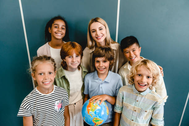 scolari compagni di classe bambini alunni studenti in piedi con l'insegnante che tiene il globo alla classe di lezione della scuola di geografia. eco-attivisti. protezione dell'ambiente. concetto di viaggio. gruppo della società multietnica - learning child education globe foto e immagini stock