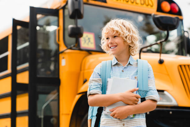 istock Young smiling kid boy going back to school study education learning holding copybooks and notebooks standing next to the school bus. New educational year, semester after lockdown quarantine. 1338735303