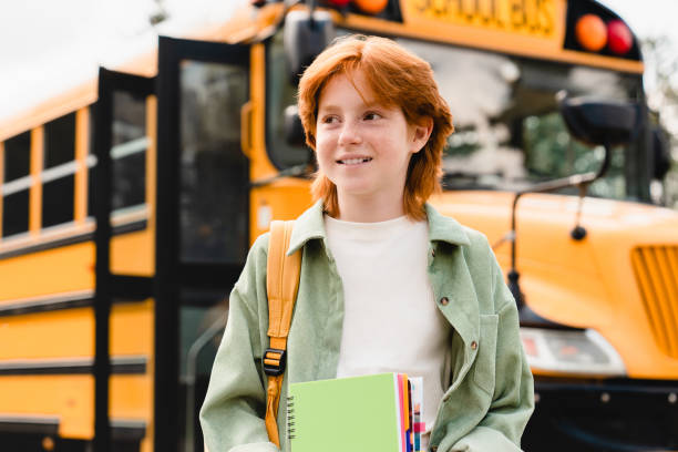 istock Redhead young student kid schoolchild pupil preparing for school, coming back to learning after summer holidays holding notebooks and copybooks close to school bus 1338736141