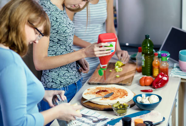 Friends Preparing Pizza for a Dinner Party Three young women preparing food together in modern kitchen college dorm party stock pictures, royalty-free photos & images