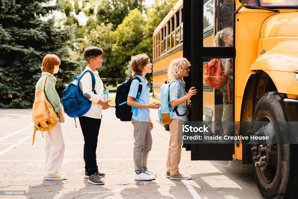 Multiethnic mixed-race pupils classmates schoolchildren students standing in line waiting for boarding school bus before starting new educational semester year after summer holidays Back to School Stock Photo
