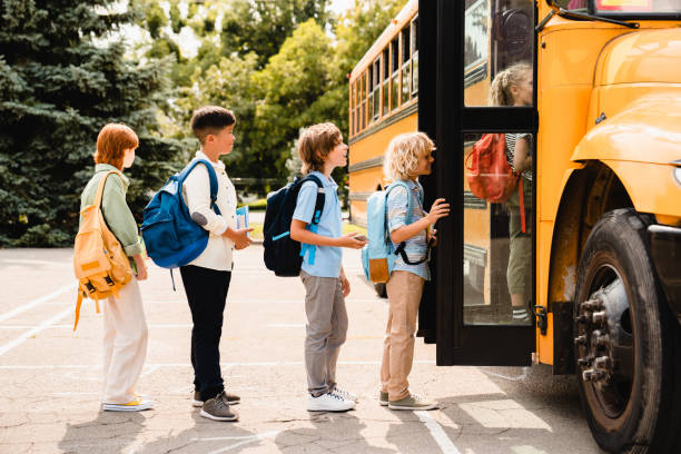Multiethnic mixed-race pupils classmates schoolchildren students standing in line waiting for boarding school bus before starting new educational semester year after summer holidays stock photo