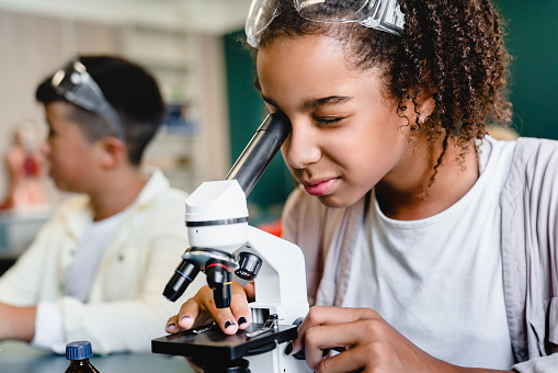 Estudiante de una alumna afroamericana que trabaja con microscopio en la clase de lección de química de biología en el laboratorio de la escuela. Concepto de lección de ciencia photo