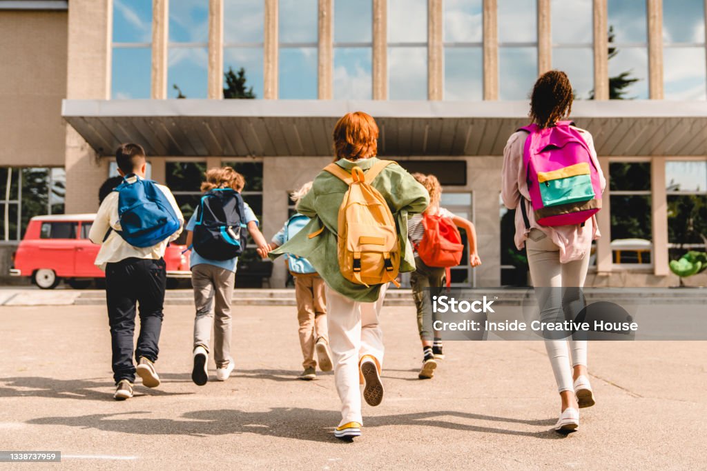 Little kids schoolchildren pupils students running hurrying to the school building for classes lessons from to the school bus. Welcome back to school. The new academic semester year start Education Stock Photo