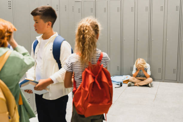 istock Lonely sad schoolboy crying at the school hall floor while his classmates ignoring him. Bullying at school problem. Social excluding concept 1338738952
