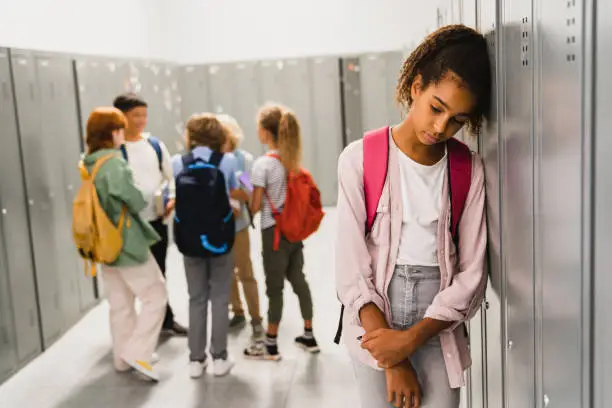 Lonely sad african-american schoolgirl crying while all her classmates ignoring her. Social exclusion problem. Bullying at school concept. Racism problem