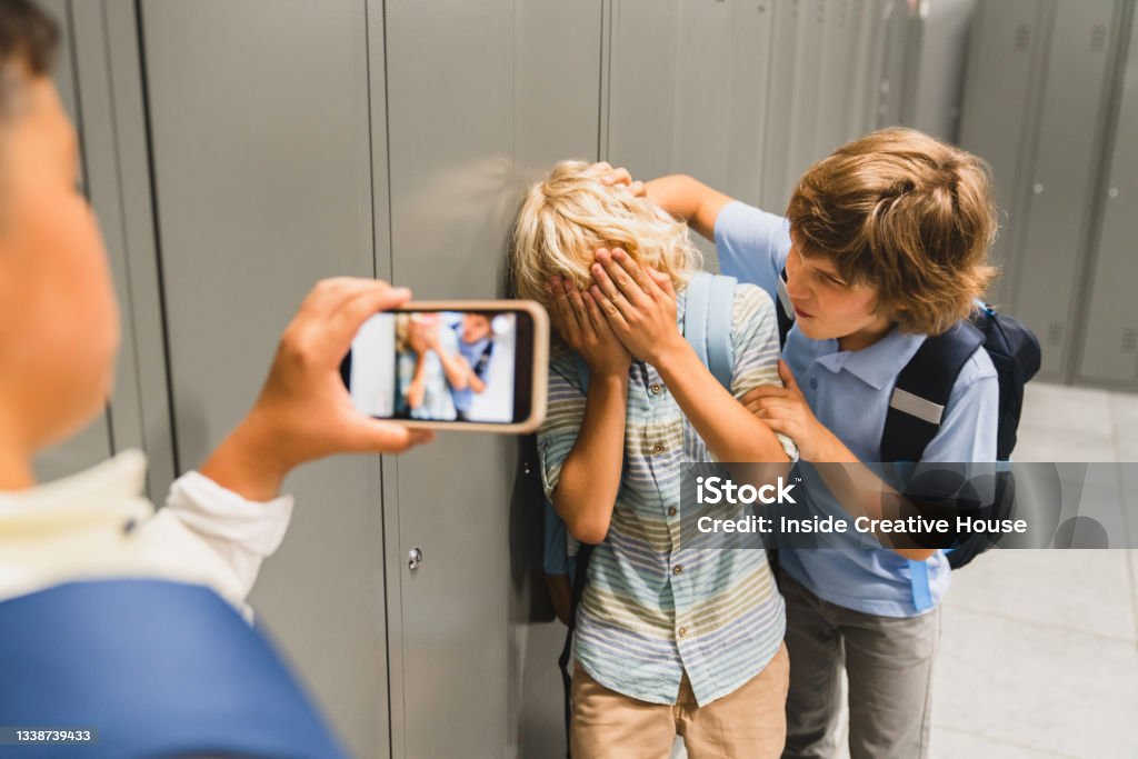 Schoolchildren cruel boys filming on the phone torturing bullying their classmate in school hall. Puberty difficult age Bullying Stock Photo