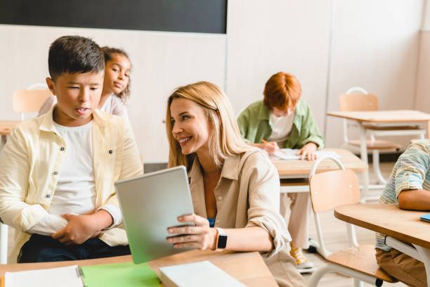istock Young teacher tutor helping her students schoolchildren pupils with homework task math exam test at the school lesson class using digital tablet. 1338740147