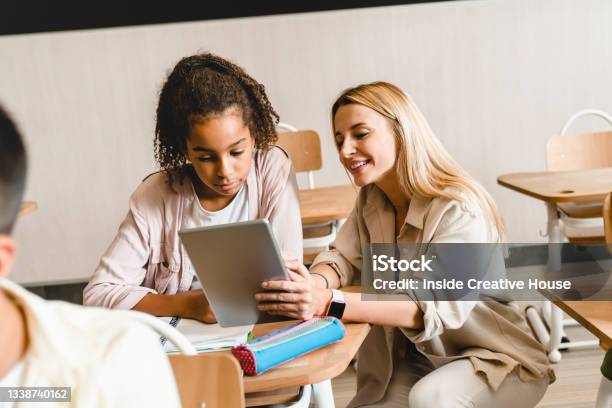 Young Teacher Tutor Helping Africanamerican Girl Students Schoolchildren Pupils With Homework Task Math Exam Test At The School Lesson Class Using Digital Tablet Stock Photo - Download Image Now