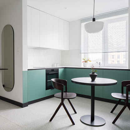 Stylish apartment with modern white and mint green kitchen with black dining table and two chairs and trendy oval mirror