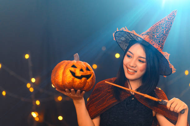 portrait of beautiful young woman in witch halloween costume wear witches hat hold pumpkin jack o lanterns and magic wand over spooky dark magic background - halloween party concept. - witch beauty beautiful women imagens e fotografias de stock