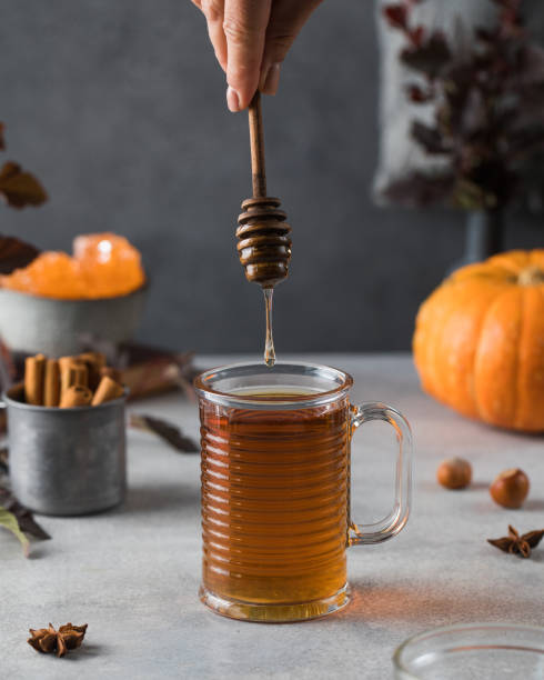 Woman adds honey to fresh hot tea on grey stone table Woman adds honey to fresh hot tea in glass cup with metal dipper on grey stone table with different ingredients close view glass cup of boiling water stock pictures, royalty-free photos & images