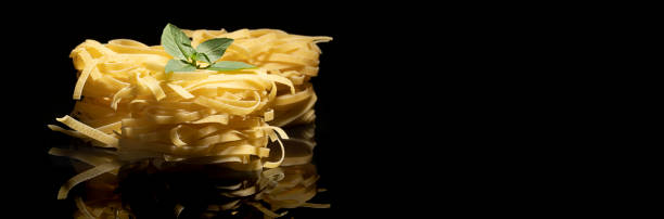 Raw tagliatelle pasta on black background
